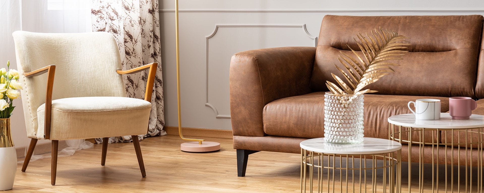 Panoramic view of living room with two small coffee tables, vintage armchair and brown leather sofa, real photo